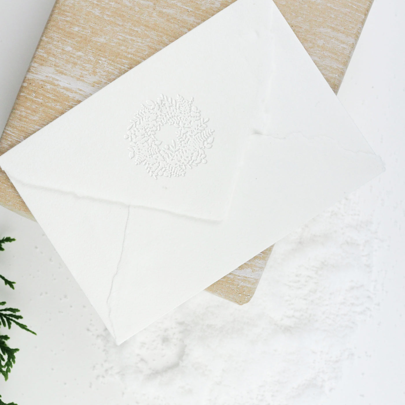 White envelope flap embossed with 3D Christmas wreath on a wrapped gift and snow | Heirloom Seals