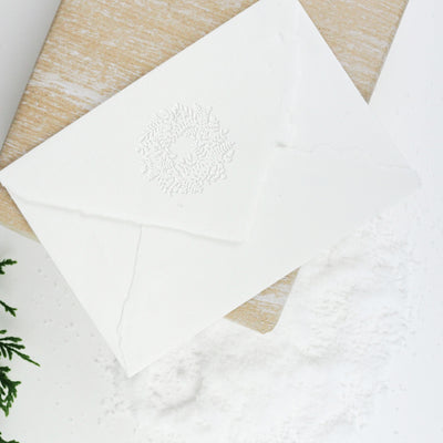 White envelope flap embossed with 3D Christmas wreath on a wrapped gift and snow | Heirloom Seals