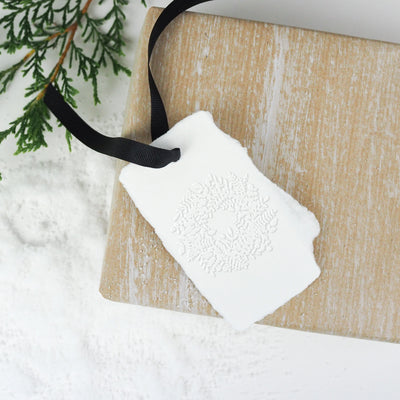 Christmas wreath embossed gift tag tied with ribbon on a wooden board and bed of snow | Heirloom Seals