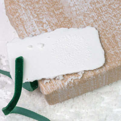 White gift tag embossed with 3D wreath on a Christmas gift and snow | Heirloom Seals