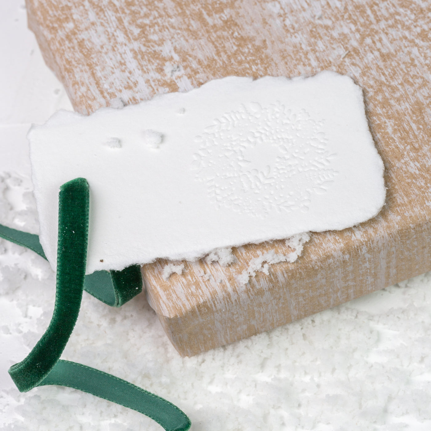 White embossed gift tag tied with velvet green ribbon on a Christmas present in a bed of snow | Heirloom Seals
