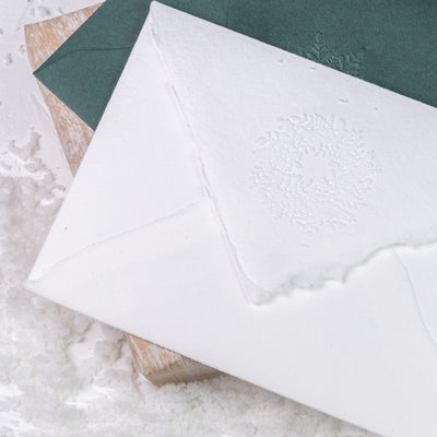 White and green envelope seals embossed with 3D Christmas wreaths on top of a gift in the snow | Heirloom Seals
