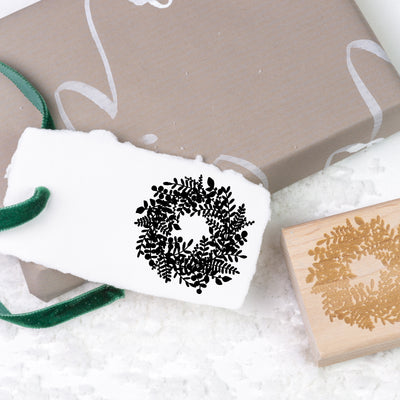 Gift tag stamped with bushy winter wreath on top of Christmas present and snow | Heirloom Seals