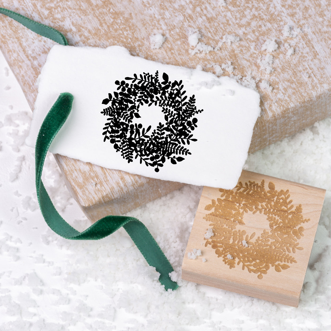 Christmas wreath gift tag tied with green velvet ribbon and wooden rubber stamp on a bed of snow | Heirloom Seals
