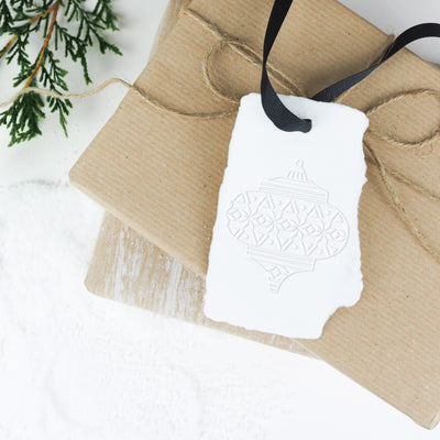 Christmas present wrapped in twine and embossed bauble gift tag on a bed of snow | Heirloom Seals