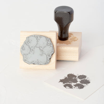 Black cat paw print impression on white paper next to custom wooden rubber stamp with handle