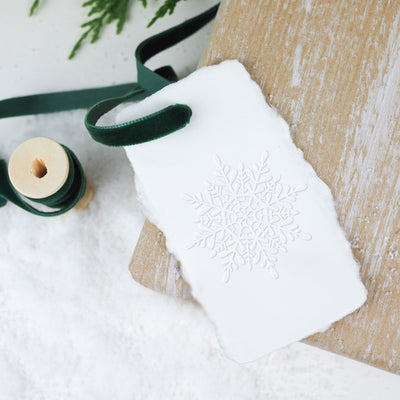 Christmas snowflake embossed gift tag tied with velvet green ribbon on a bed of snow | Heirloom Seals