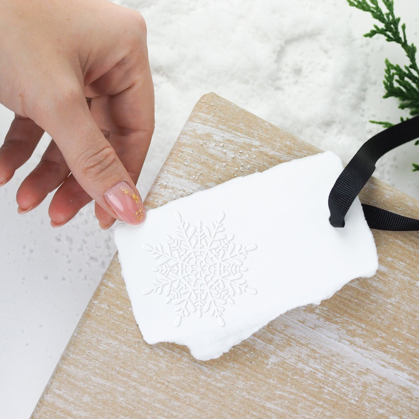 Embellishing a Christmas gift with a white snowflake-embossed gift tag and black ribbon | Heirloom Seals