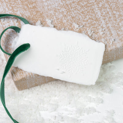 White gift tag embossed with detailed snowflake and velvet green ribbon on a bed of snow | Heirloom Seals
