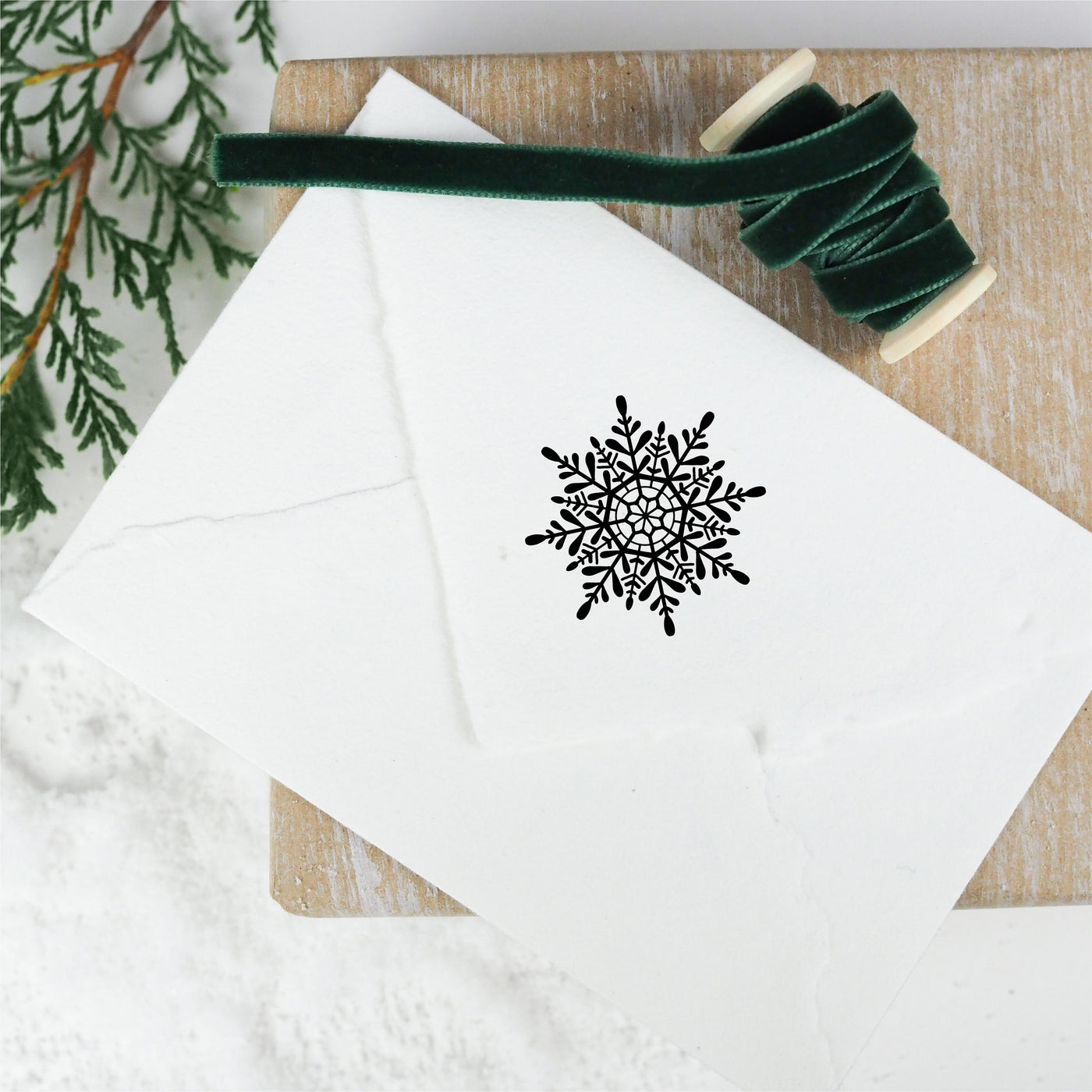White envelope seal stamped with Christmas snowflake on wooden board with green ribbon | Heirloom Seals