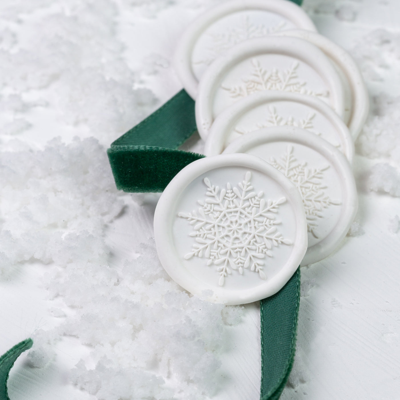 White snowflake self-adhesive wax seals entwined in green ribbon on a bed of snow|  Heirloom Seals