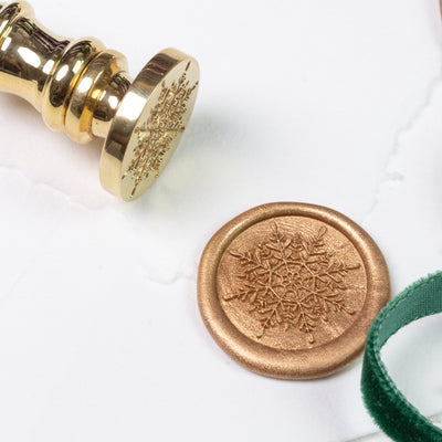 Brass snowflake wax seal stamp and hand-stamped impression on a bed of snow | Heirloom Seals