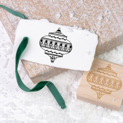 Christmas bauble gift tag tied with green velvet ribbon and wooden rubber stamp on a bed of snow | Heirloom Seals