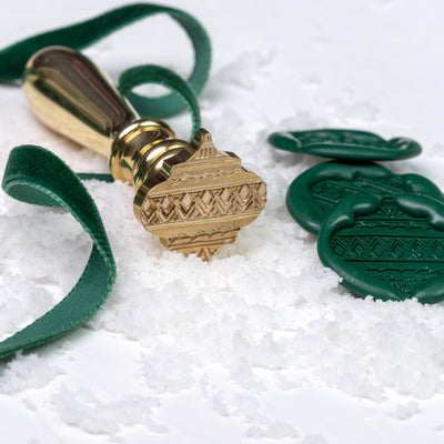 Brass bauble wax seal stamp with green wax seals on a bed of snow | Heirloom Seals